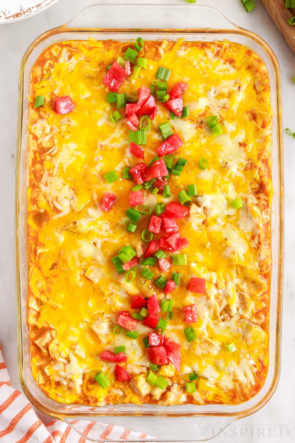 vertical full view picture of turkey enchilada casserole topped down the center with green onions and tomatoes