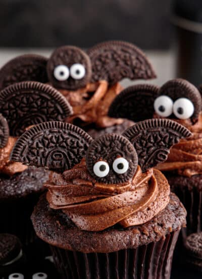 Chocolate cupcakes decorated with bats made from Oreo cookies and candy eyeballs.