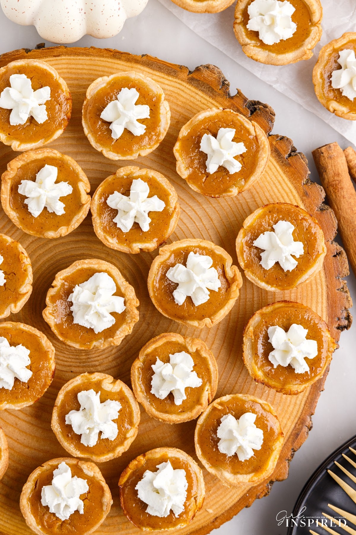 Wooden tray filled with mini pumpkin pies with whipped cream squirts on top of each one.