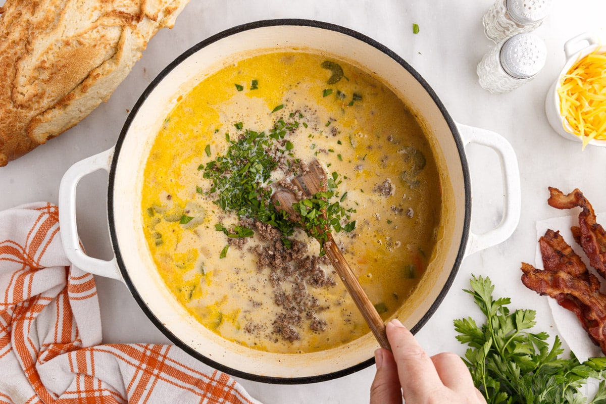 parsley stirred into bacon cheeseburger soup with a wooden spoon in a large pot