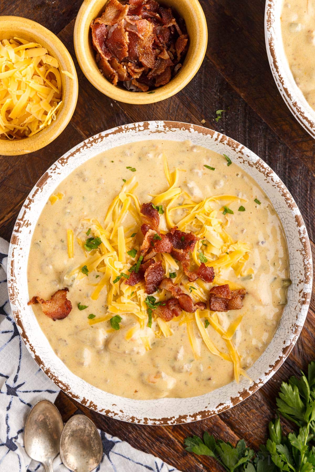 top view of a bowl of bacon soup topped with bacon and cheese next to small bowls of bacon and cheese