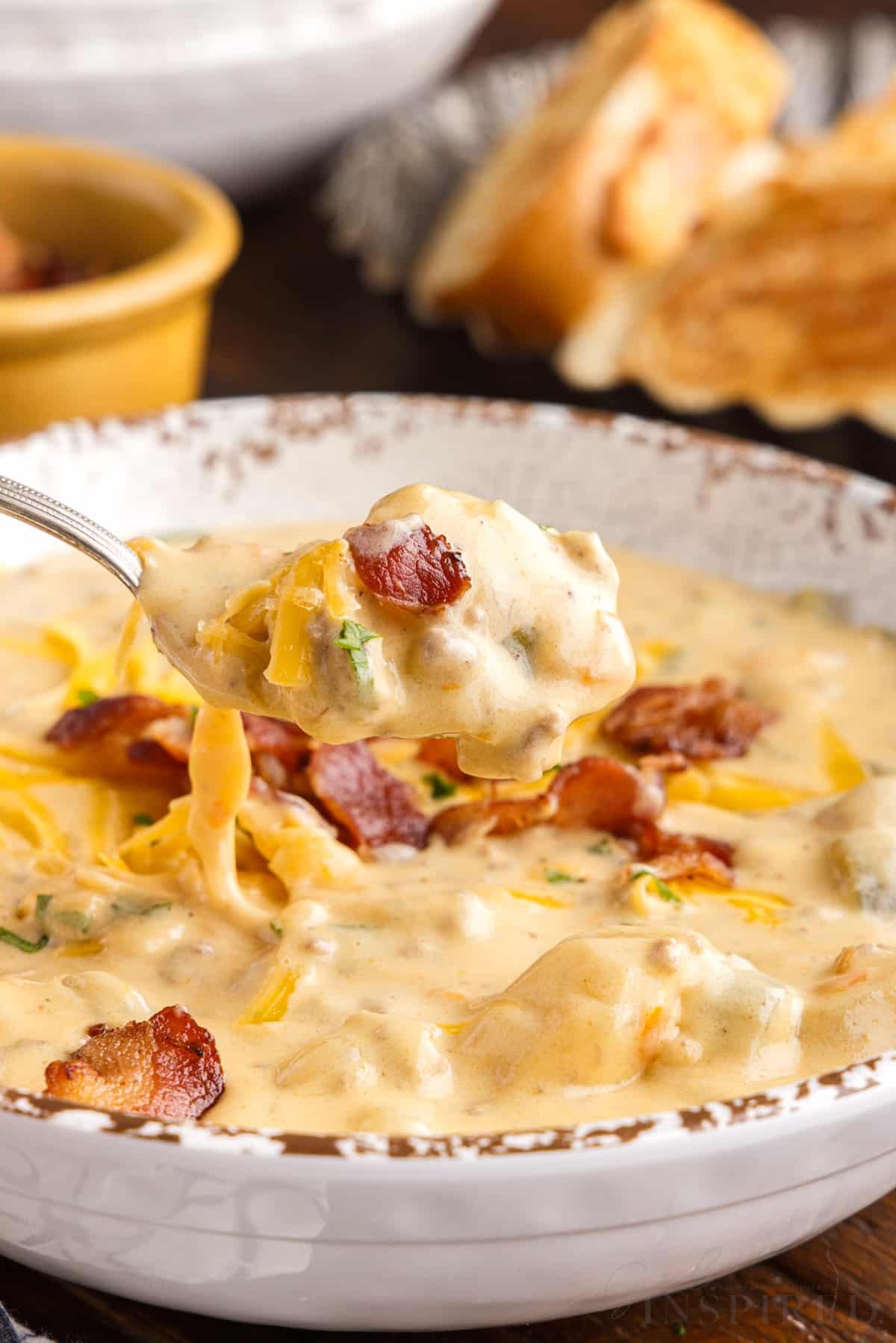 front close up of a spoon of bacon cheeseburger soup lifted over a bowl of soup