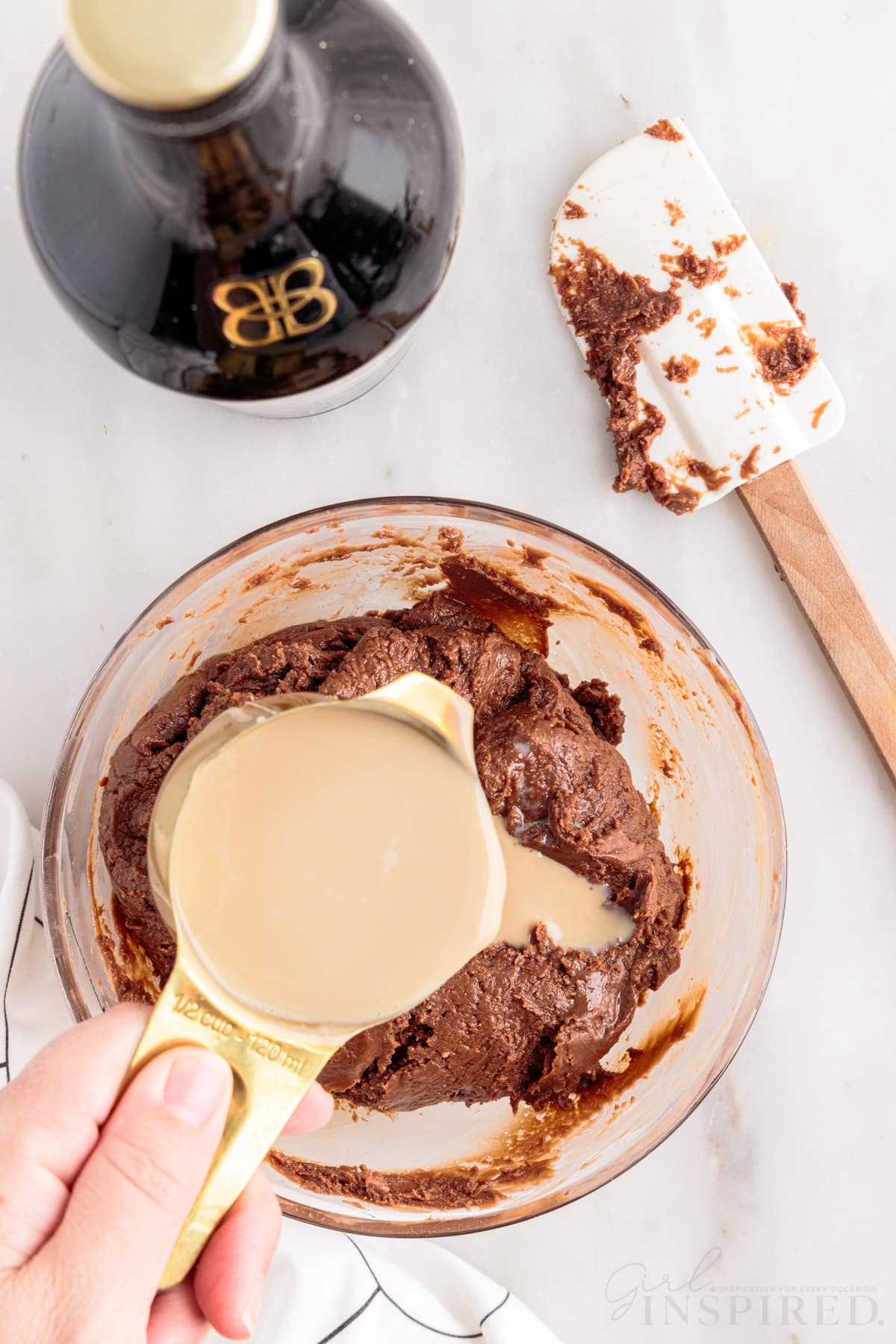 a cup of irish cream over melted chocolate chip mixture next to a spatula and baileys bottle