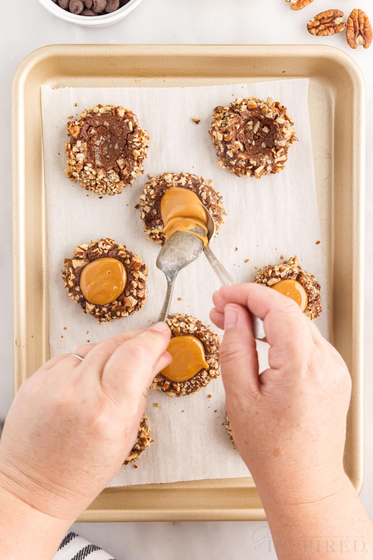 two spoons adding melted caramel to baked chocolate turtle thumbprint cookies