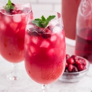 Christmas punch in two glasses, bowl of cranberries, jug of juice, pitcher with Christmas punch, on a marble countertop.