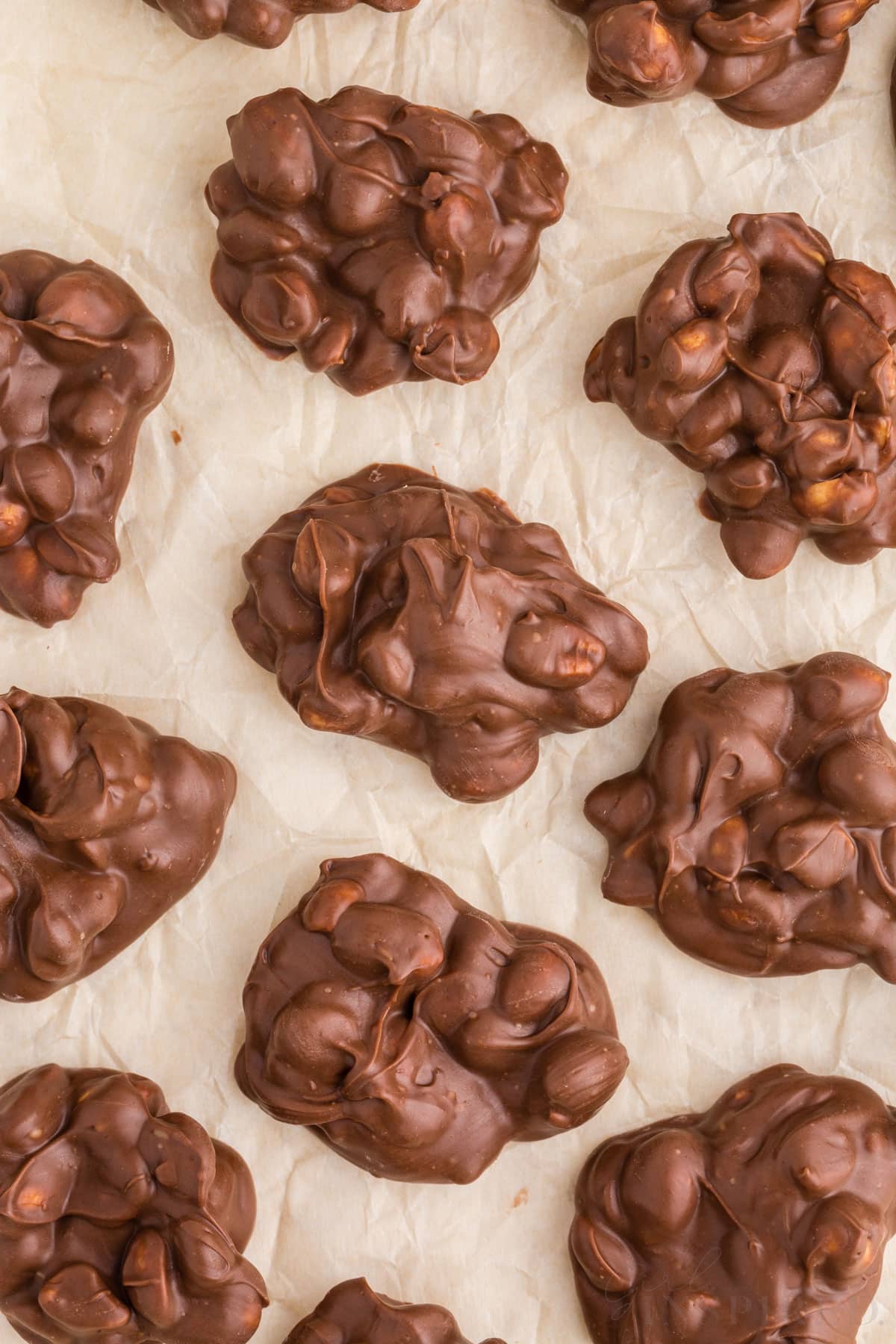 Close up of chilled chocolate peanut clusters on a tray lined with parchment paper.