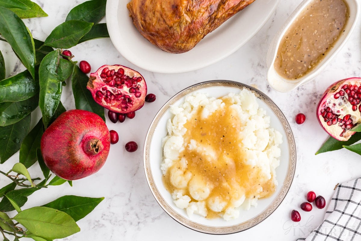 gravy poured over mashed potatoes with pomegranates, turkey and gravy boat set around.