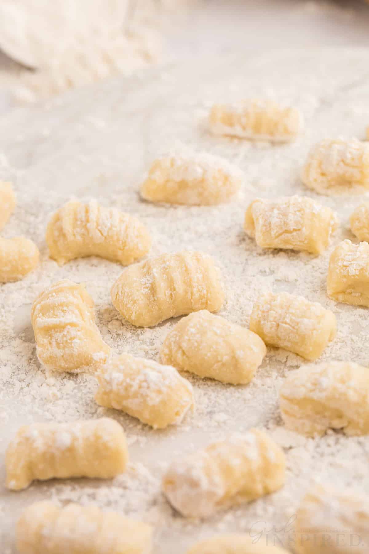 Close up of homemade gnocchi on a marble surface, loose flour in the background.