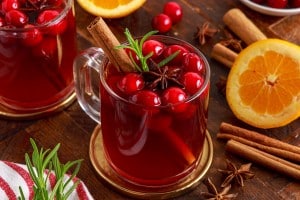 glass mug of hot cranberry drink next to oranges and cinnamon sticks