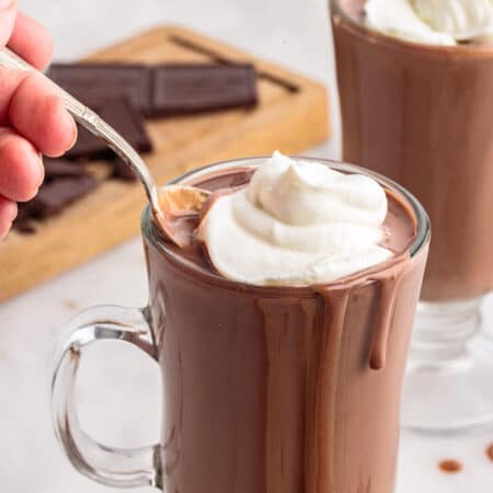 Glass mug of Italian hot chocolate topped with whipped cream with a spoon in it.