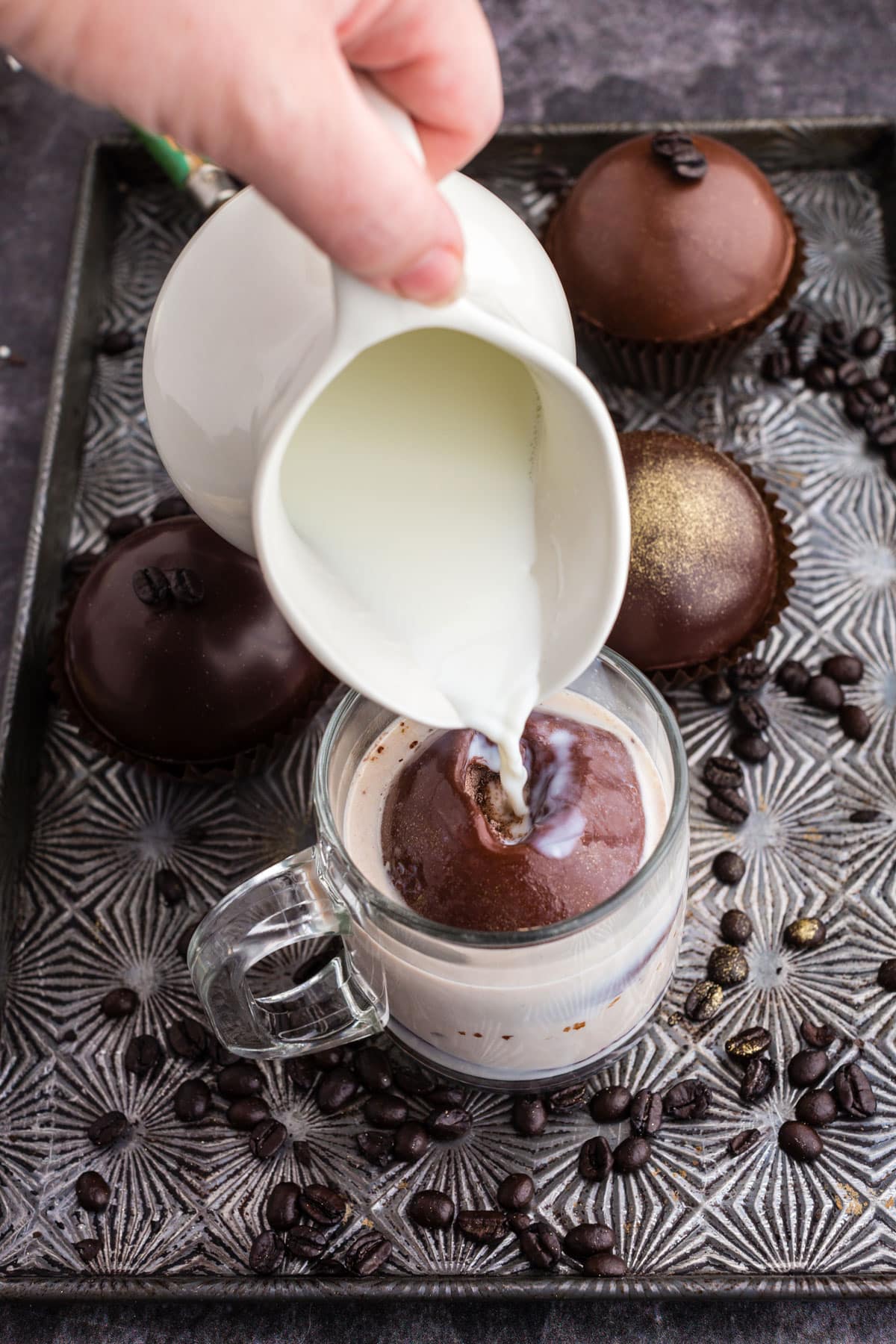 milk poured over mocha hot chocolate bomb on a cookie sheet with coffee beans