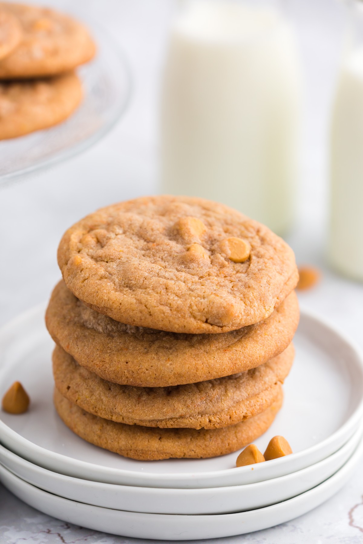 stack of pumpkin butterscotch chip cookies on white plates with milk in background.