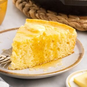 Thick slice of buttermilk cornbread on a plate, with a pat of butter and honey running down the sides.