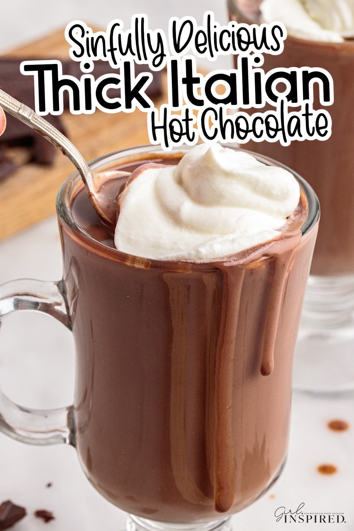 Glass mug of Italian hot chocolate topped with whipped cream with a spoon in it, and text overlay.