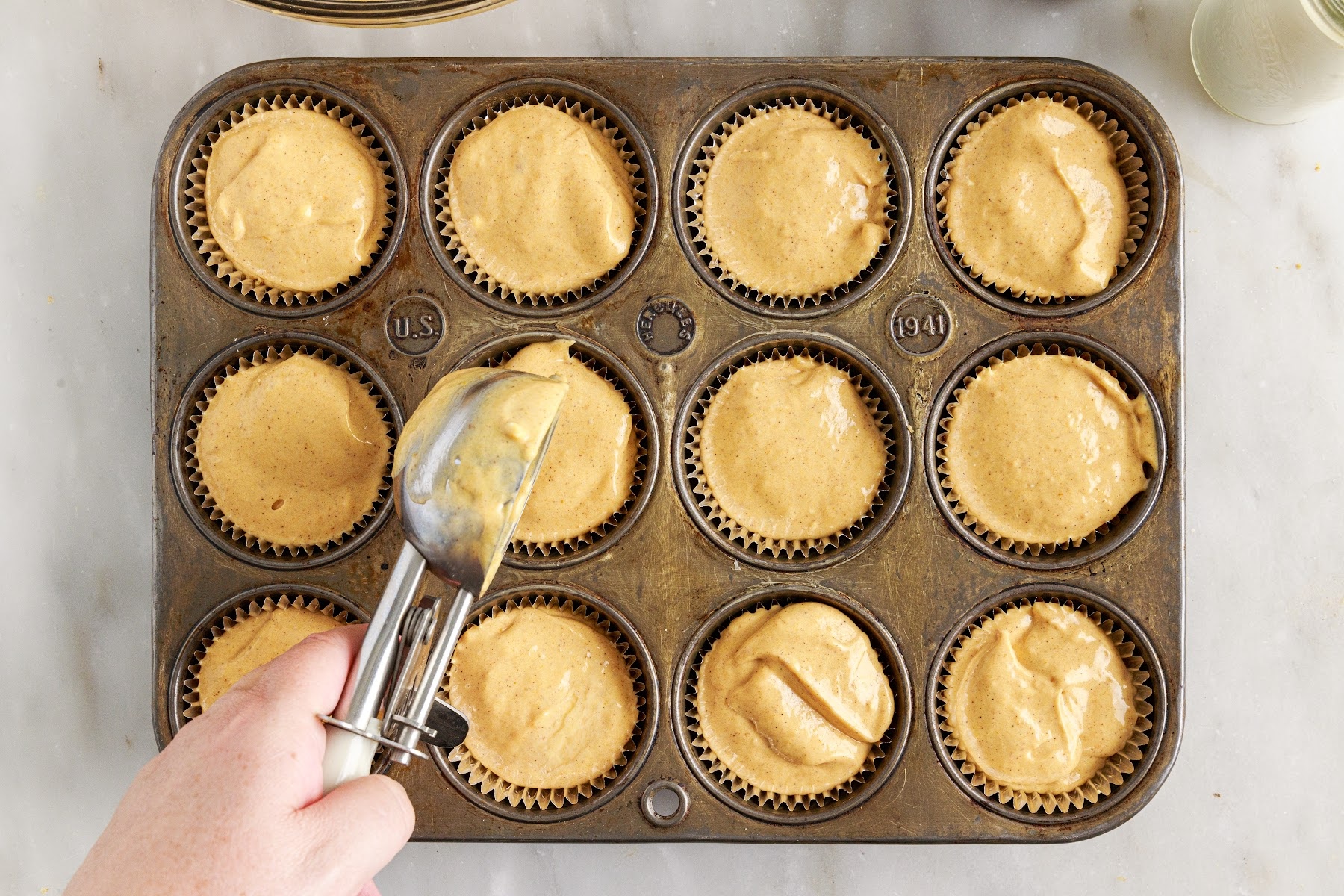 Scooping pumpkin cheesecake mixture into muffin tins.