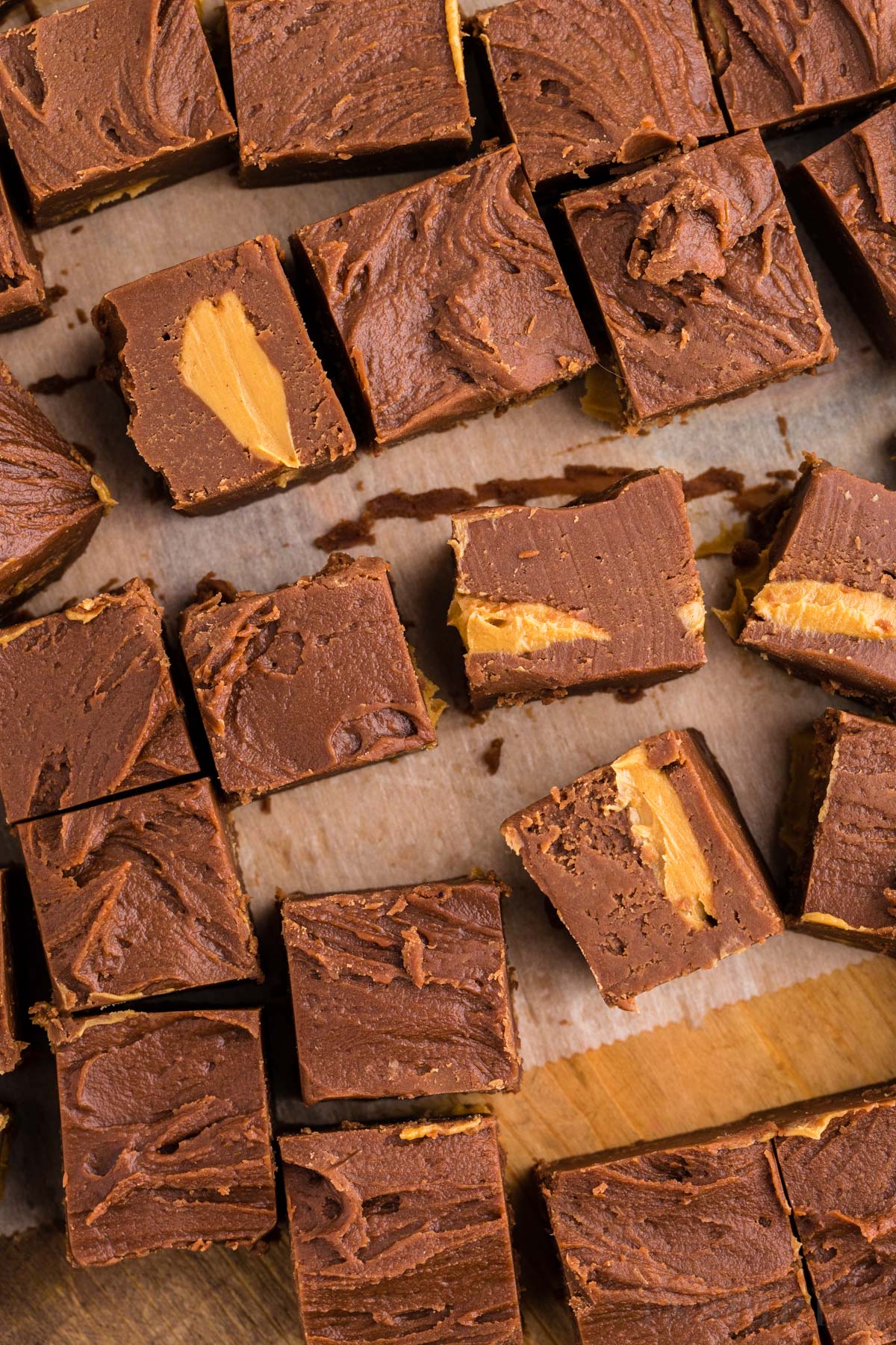 Overhead shot of pieces of chocolate peanut butter fudge on a parchment paper-lined wooden kitchen board.