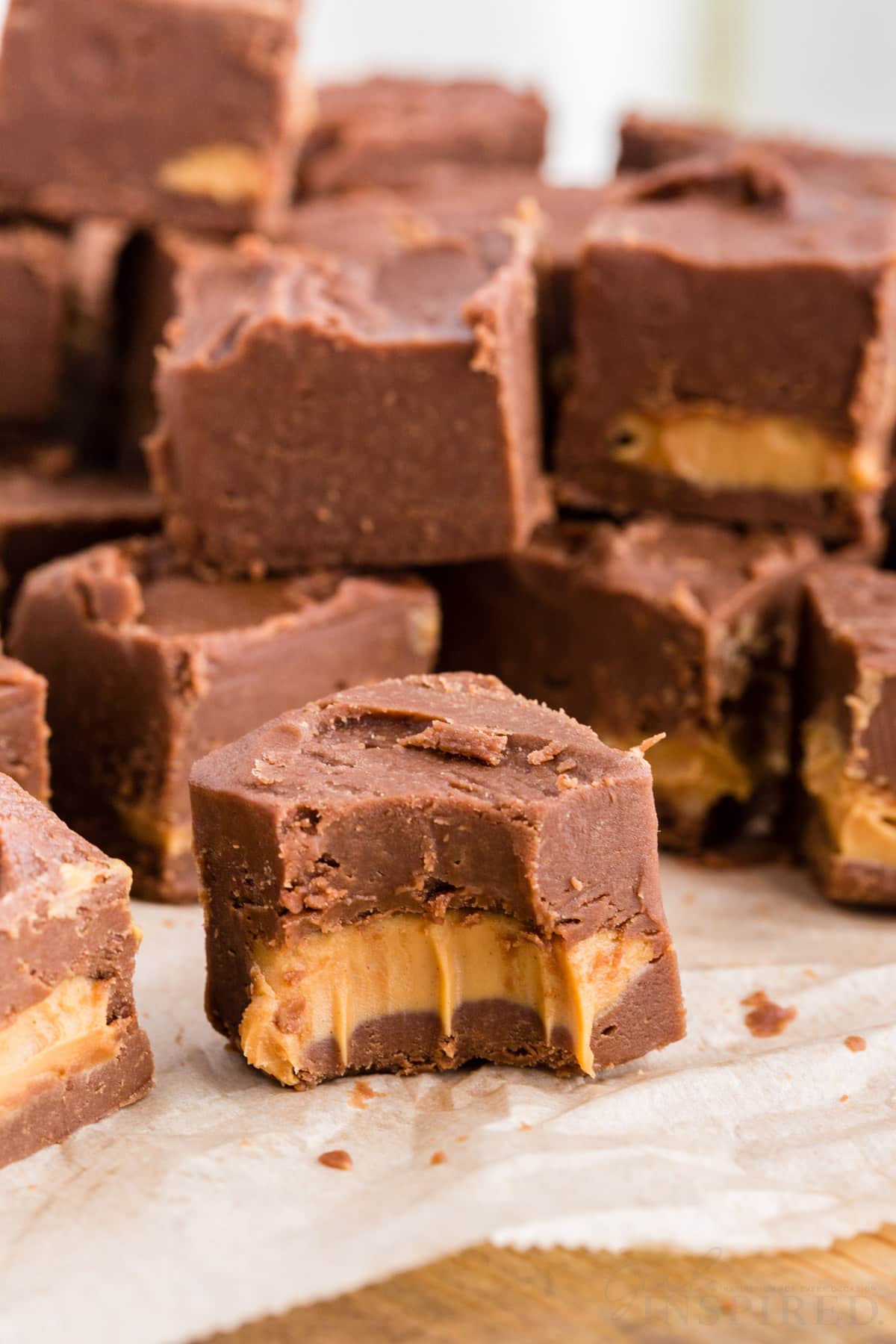 Pieces of chocolate peanut butter fudge on a parchment paper-lined wooden kitchen board, piece of fudge in front with a bite taken.