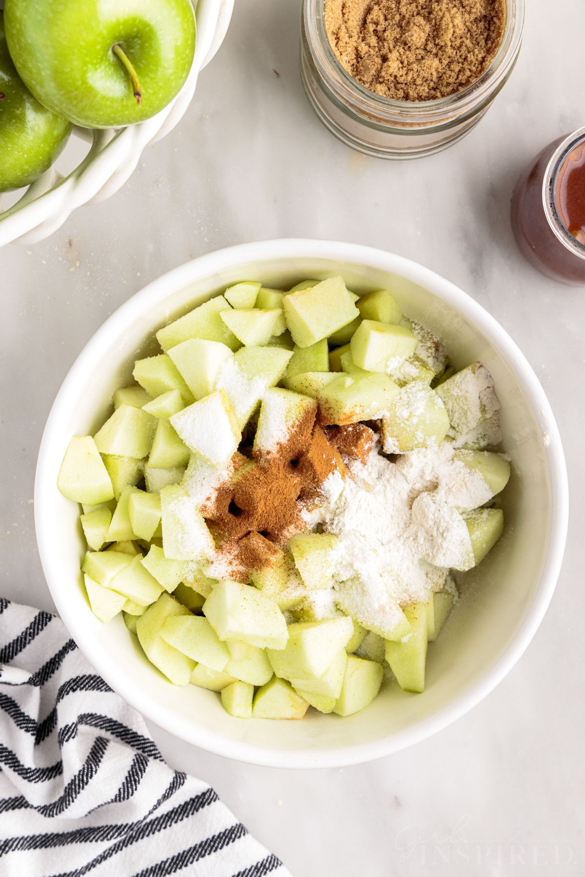 Sugar, flour, and cinnamon sprinkled over diced apples in bowl.