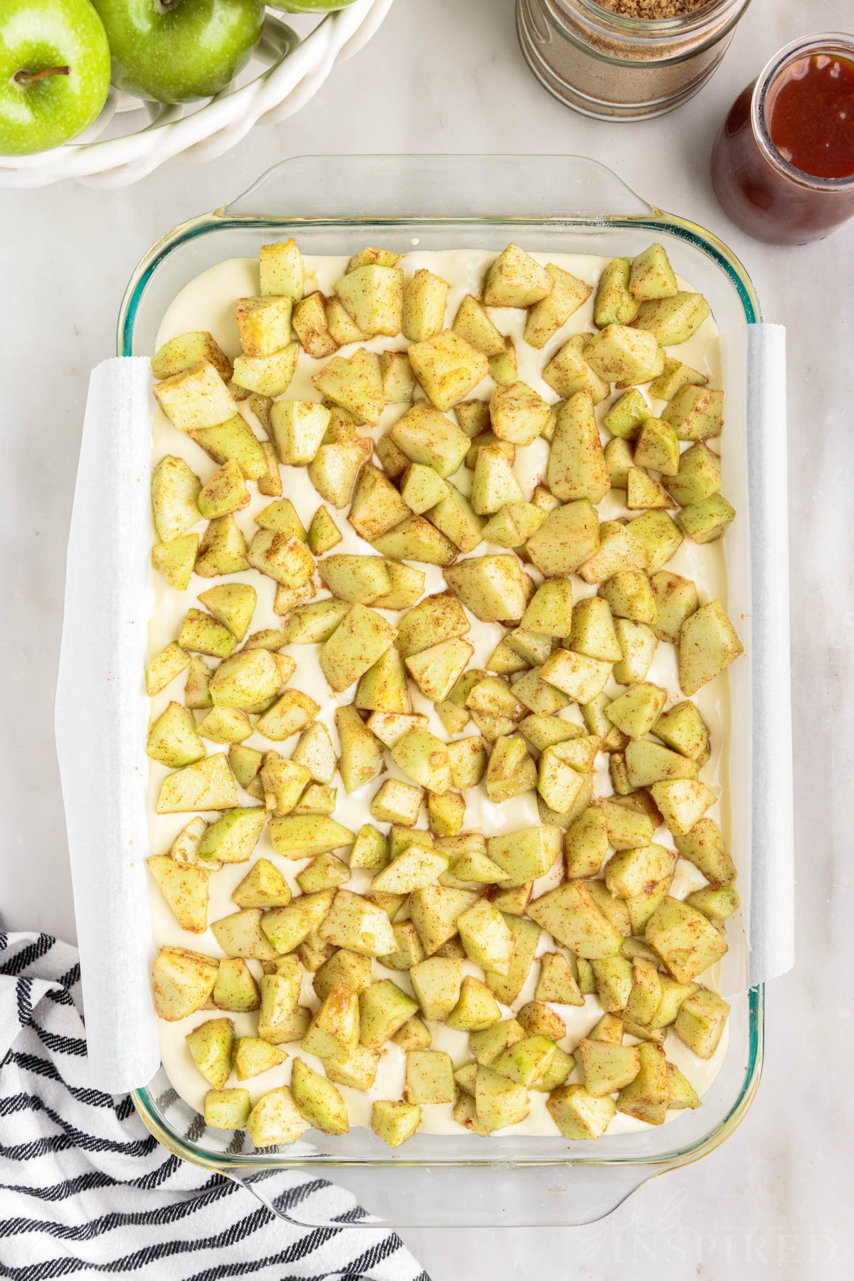Diced and seasoned apple chunks sprinkled over cheesecake filling in the baking dish.