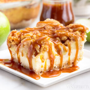 A square of apple cheesecake bar served with caramel sauce topping on a small plate, jar of caramel sauce.