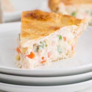 a slice of chicken pot pie on a stack of white serving plates with whole chicken pot pie in the background