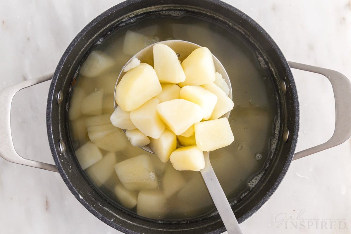 cooked potatoes for duchess potatoes on a spoon over a pot of potatoes and water