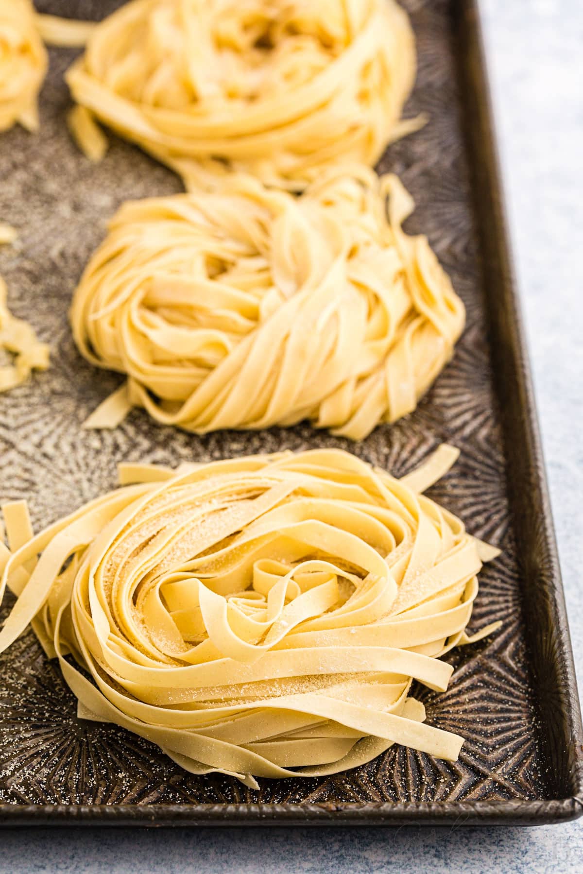 Close up of clusters of homemade pasta on a metal tray, on a marble countertop.