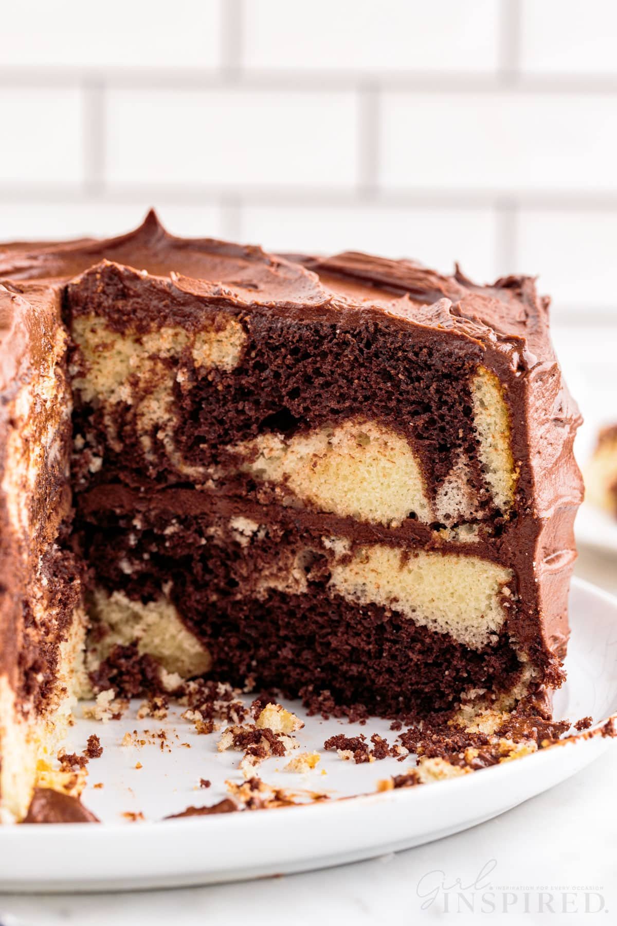 Marble cake on a white plate with two pieces removed, on a marble countertop, white stacked tiles in the background.