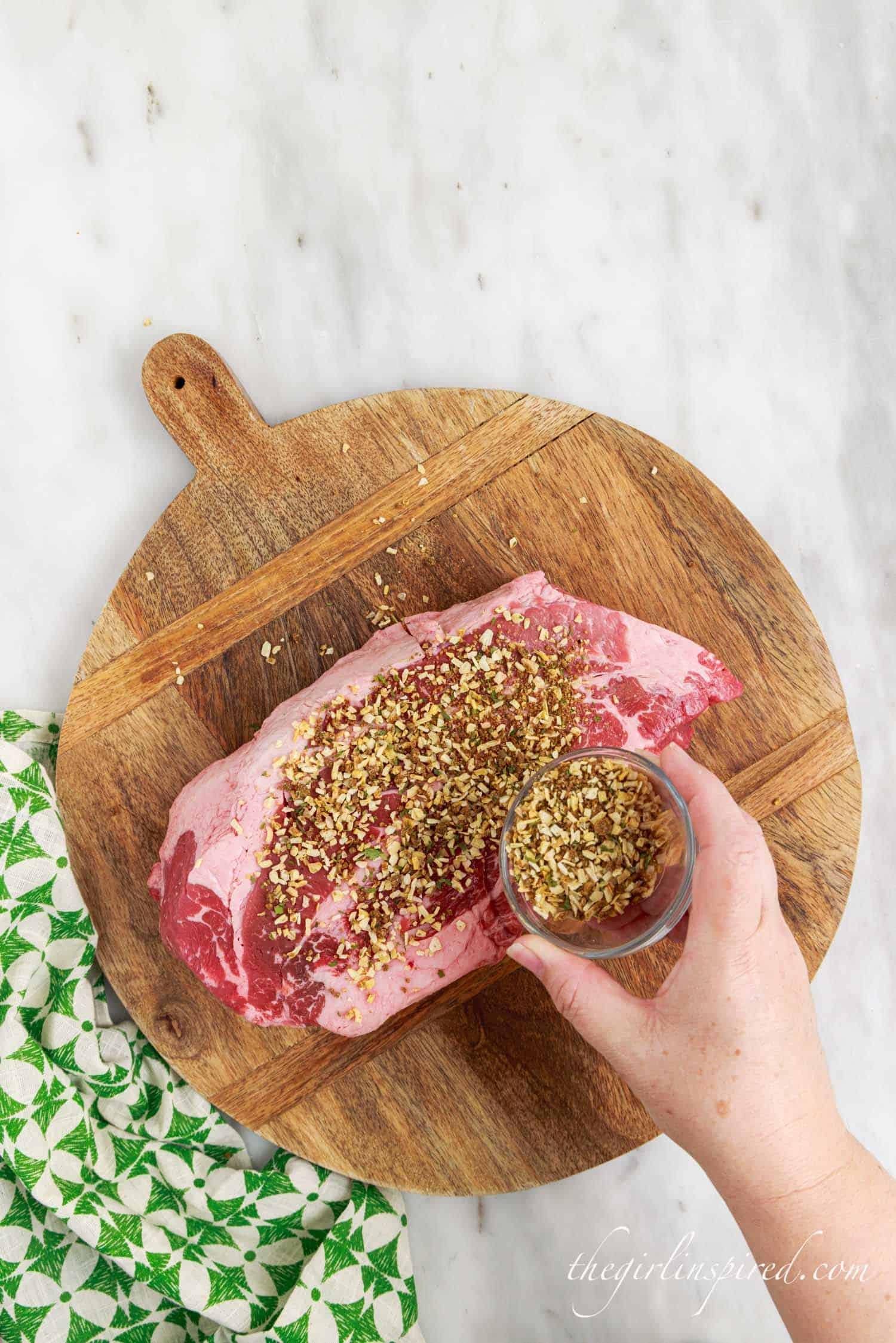 seasoning added to meat on a round wooden cutting board