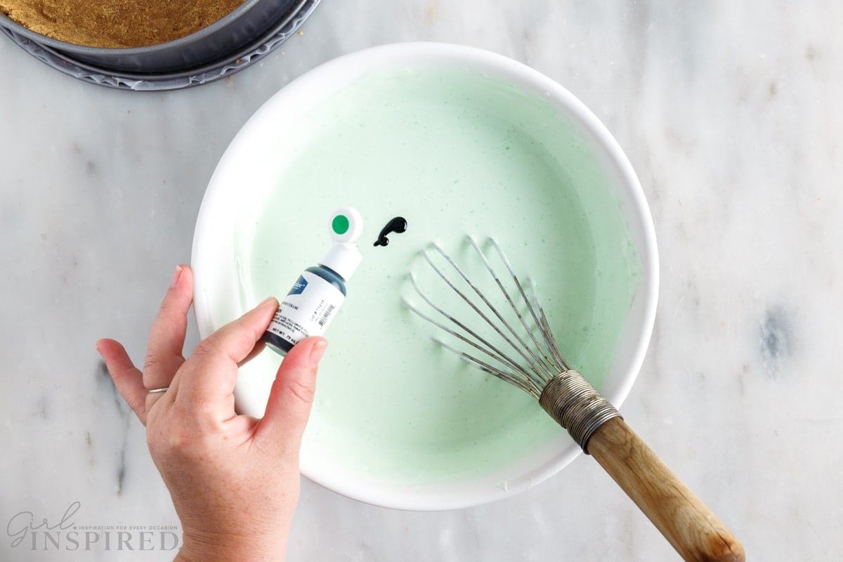 green food coloring added to jello mixture with a whisk in a mixing bowl