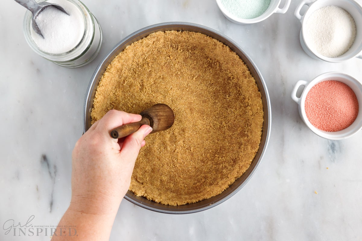 graham cracker crust being pressed into a spring form pan to make layered jello pie
