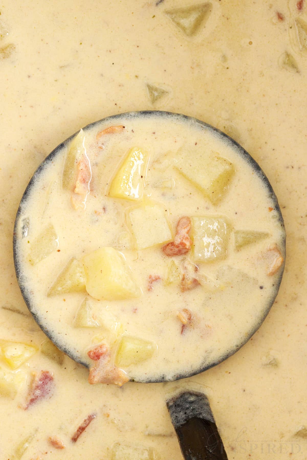 Close view of a ladle full of loaded baked potato soup lifted from the crockpot.