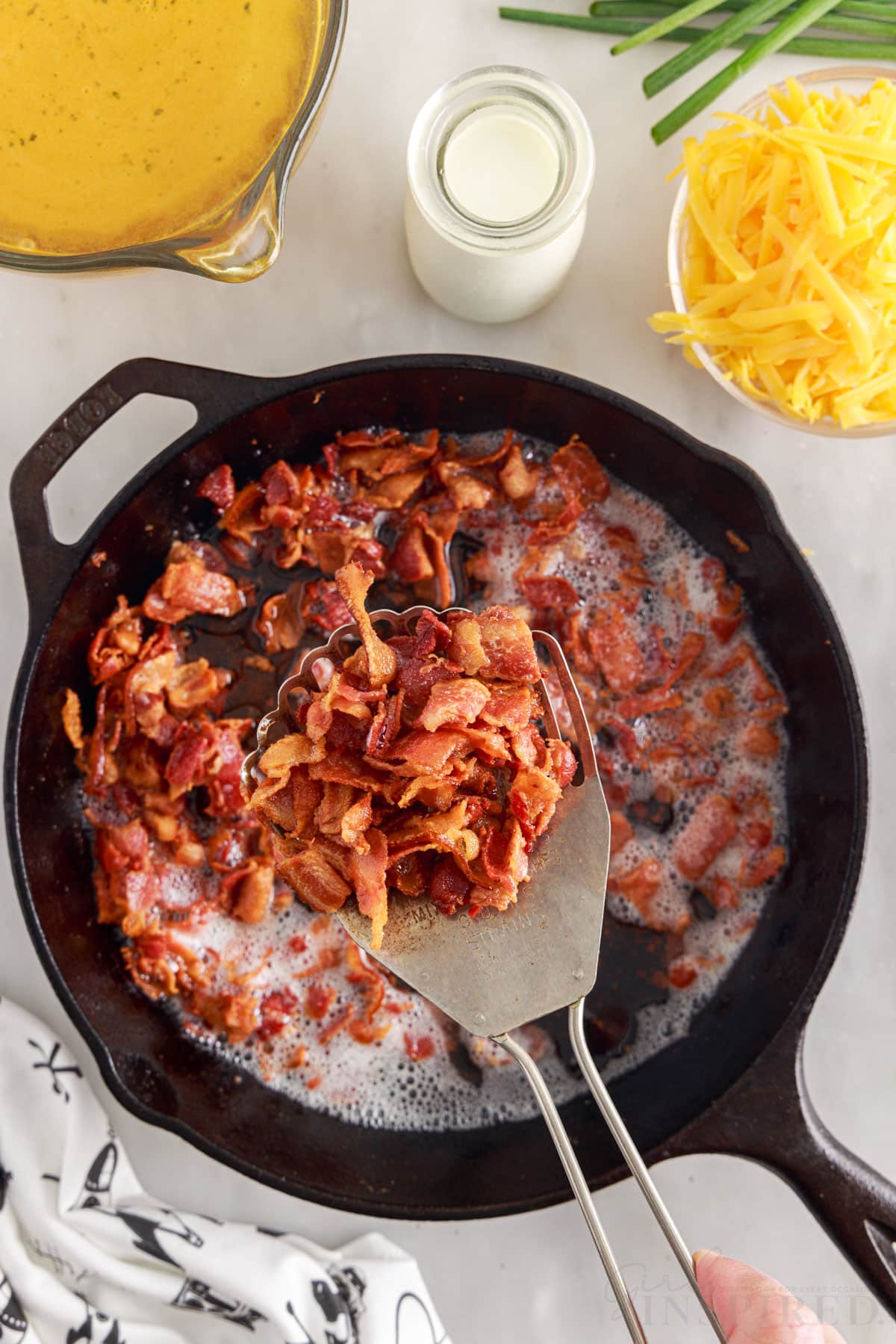 slotted spoon lifting out cooked bacon from skillet next to additional ingredients
