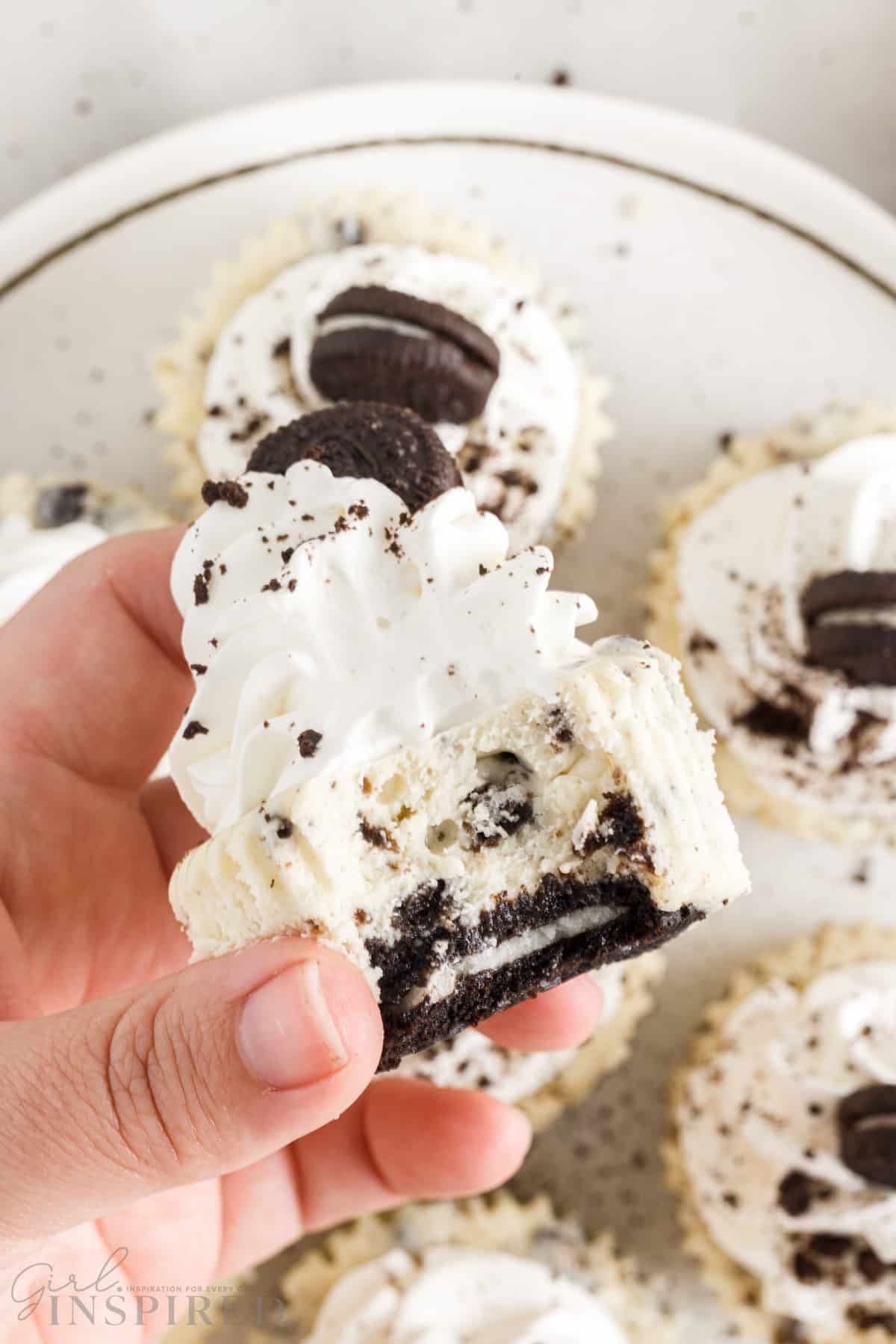 a mini oreo cheesecake being held with a slice taken from it over a plate of mini cheesecakes