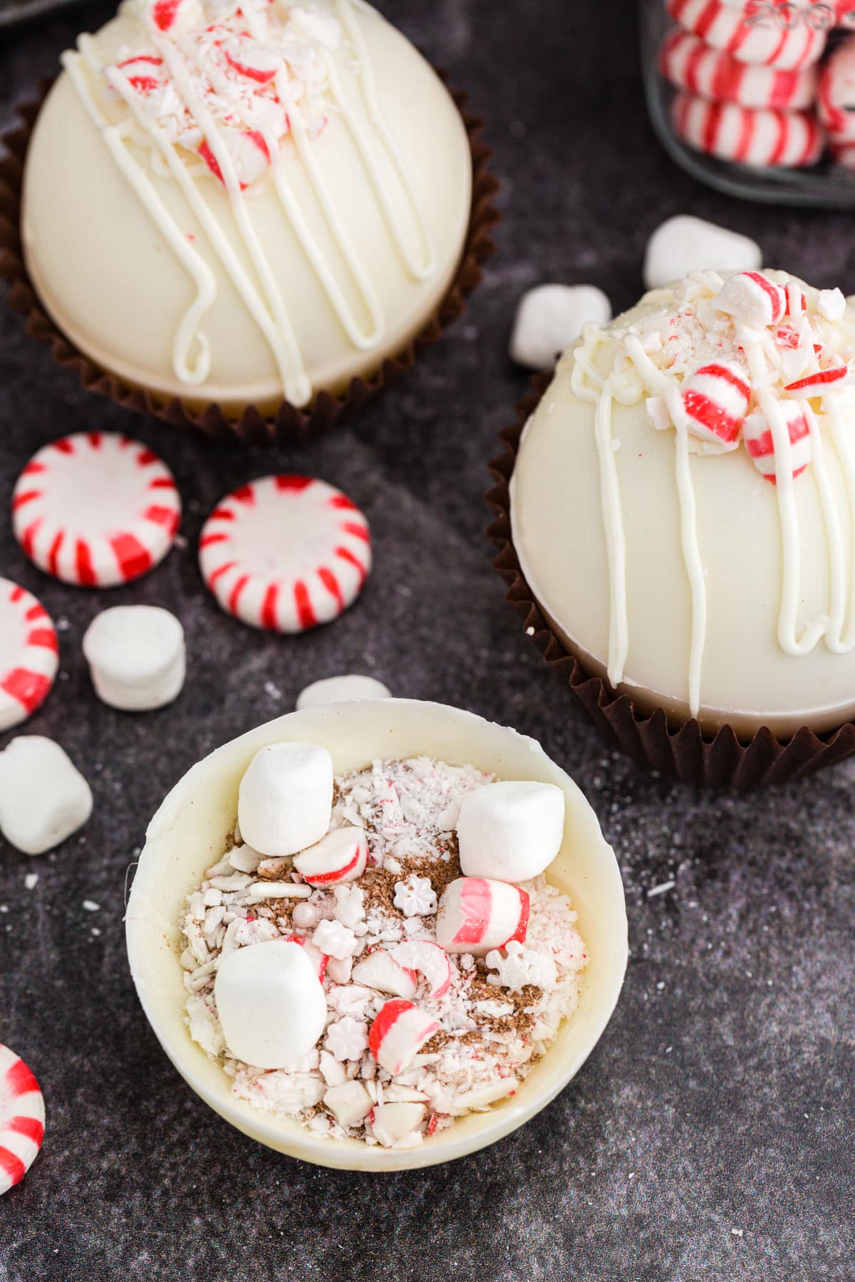 Peppermint hot chocolate spheres filled with hot chocolate, mini marshmallows, and crushed candy canes, on a dark marble countertop.