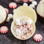 Peppermint hot chocolate bombs with hot chocolate, crushed candy canes, and mini marshmallows, on a dark marble countertop.