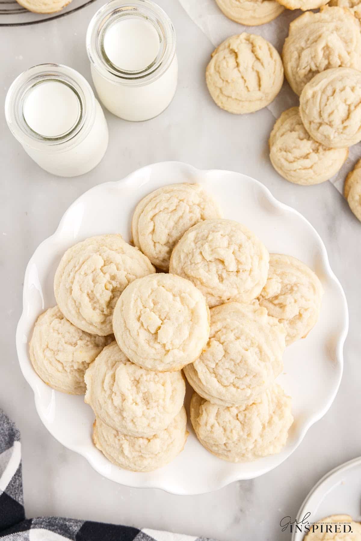 Cake stand piled with Amish sugar cookies with jars of milk and more cookies to the side.