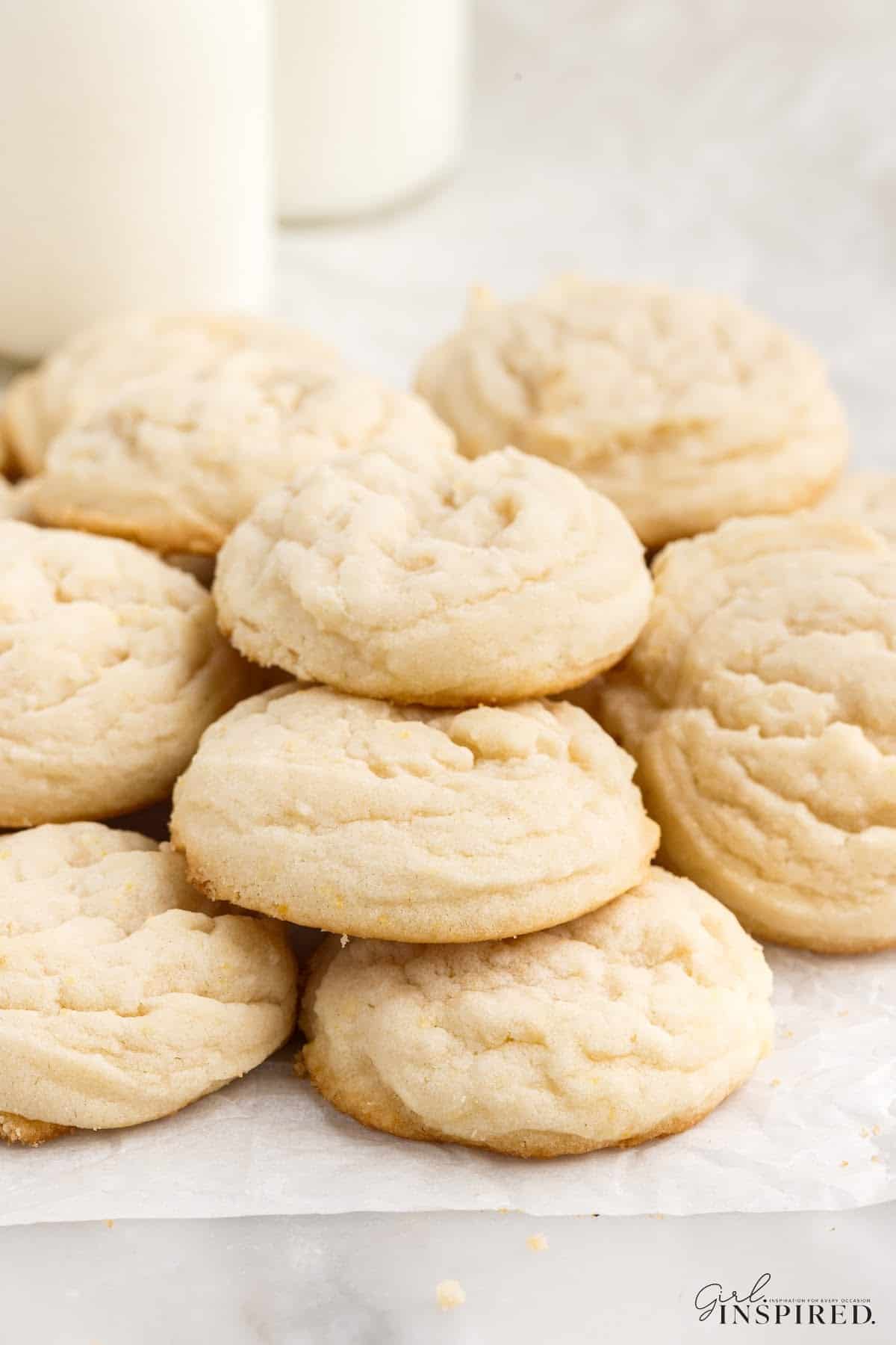 Stacked piles of Amish sugar cookies on parchment paper with milk bottles in background.