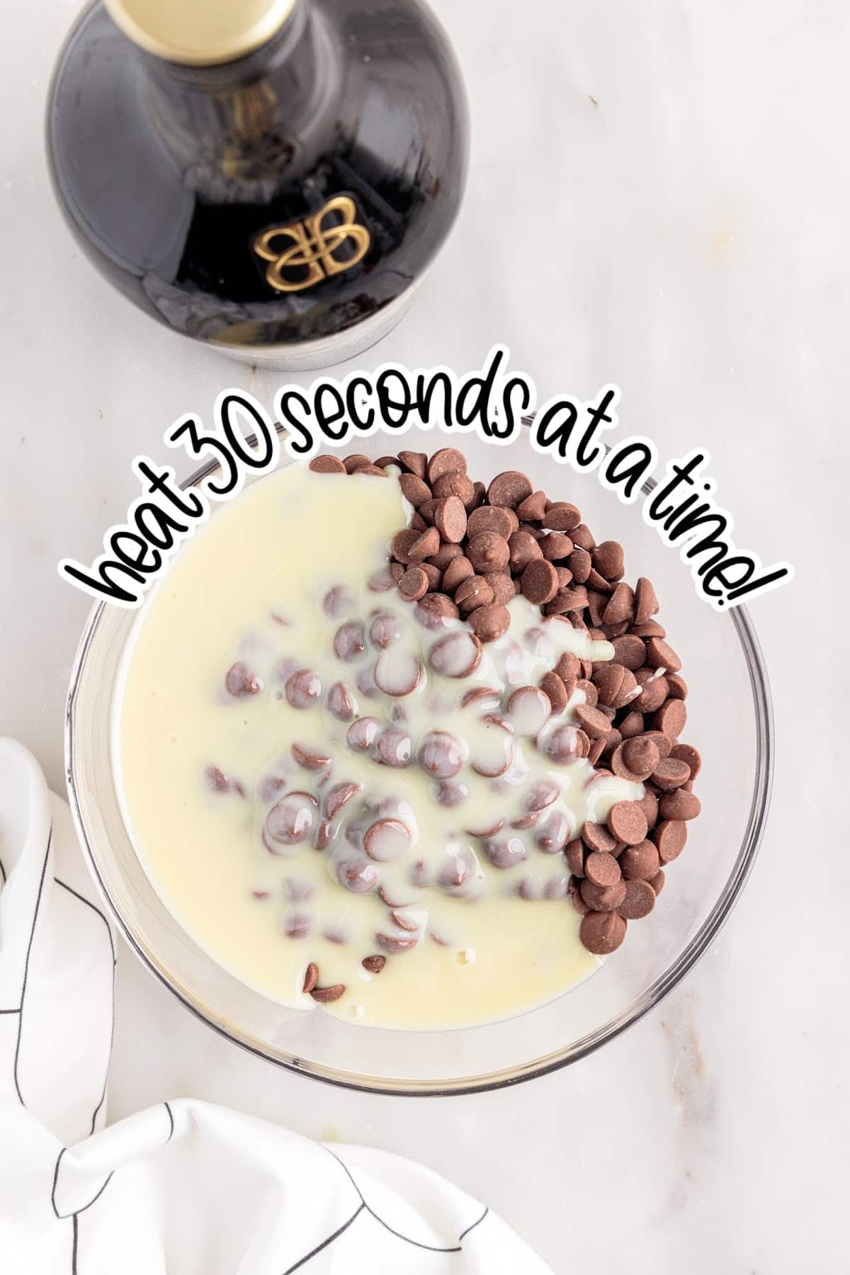 Glass bowl of condensed milk and chocolate chips with text "heat 30 seconds at a time."