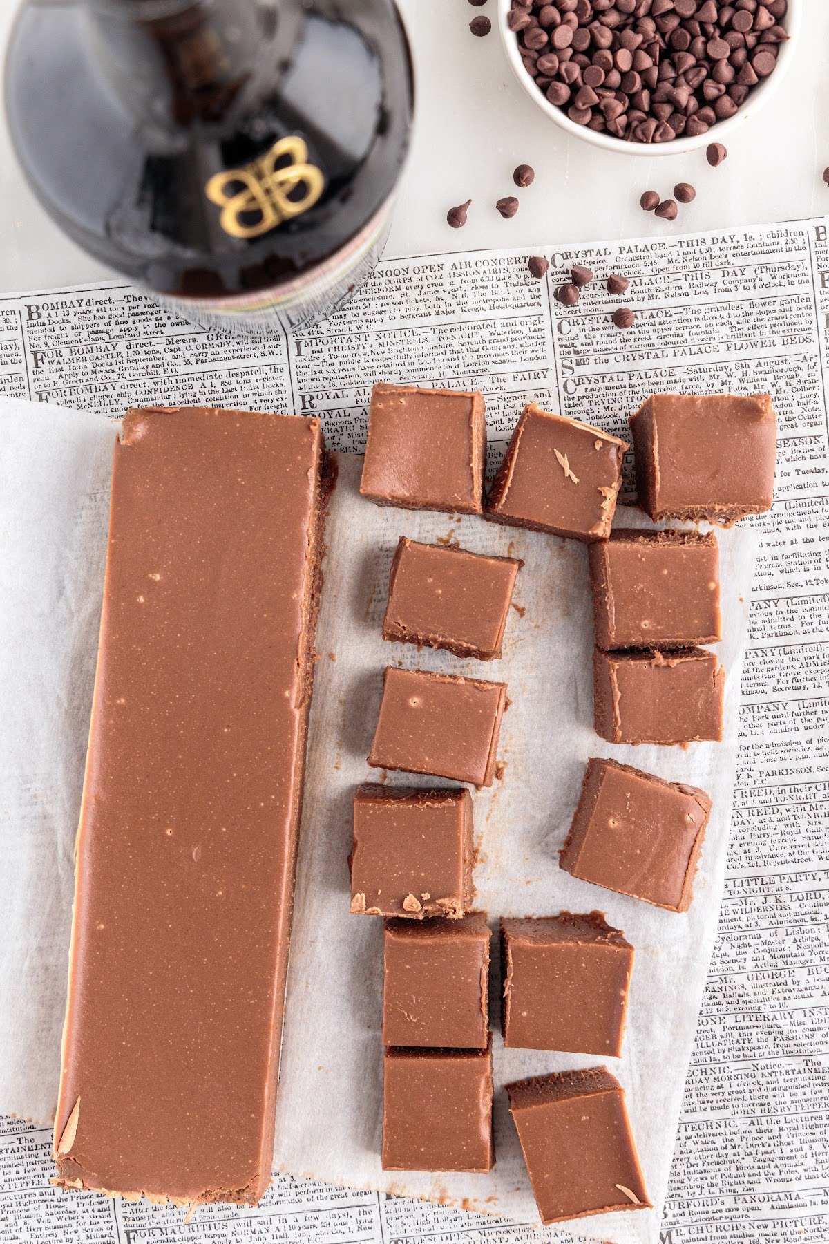 Parchment paper with block of Bailey's fudge and some of it cut into squares.