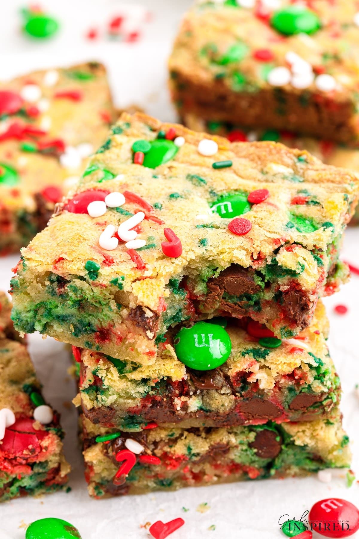 Christmas cookie bars in a stack with red and green sprinkles and M&Ms around and bite removed from top bar.