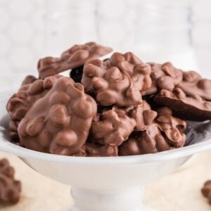 Chocolate peanut clusters on a white treat stand with parchment paper underneath, white tiles in the background.