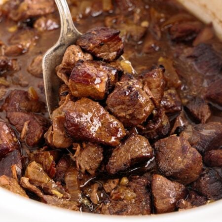 Spoon lifting cooked crockpot steak bites from crock.