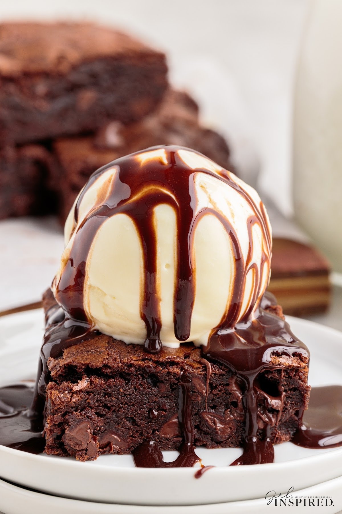 A chewy homemade brownie on a small plate topped with a scoop of ice cream drizzled with chocolate sauce.