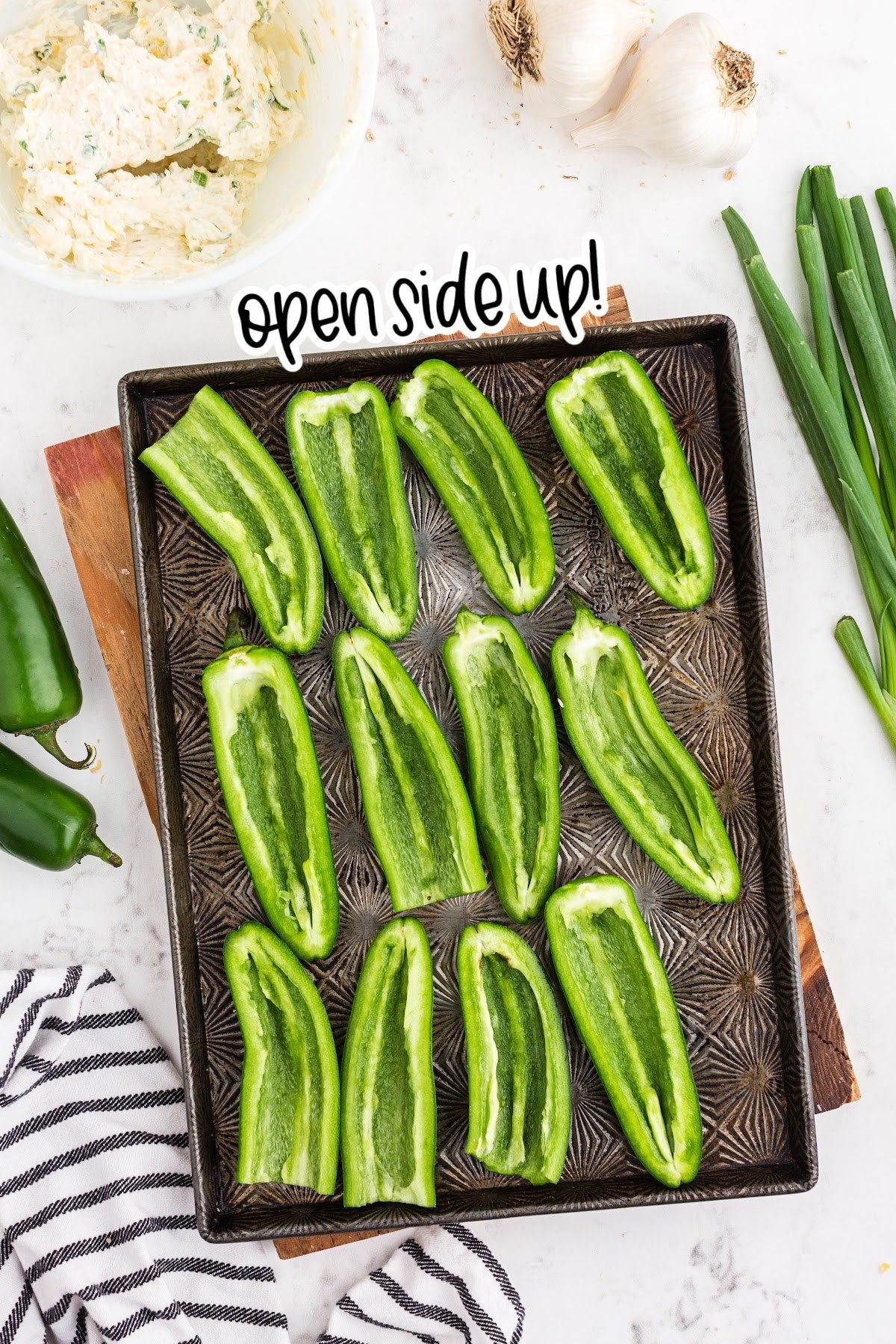 Hollowed out jalapeño peppers spread out on baking sheet with text "open side up."