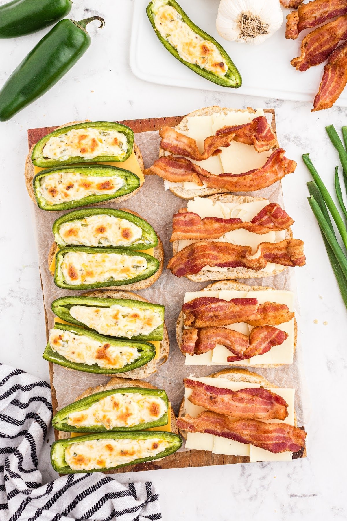 Jalapeno poppers and bacon strips stacked on top of the cheese slices on bread.