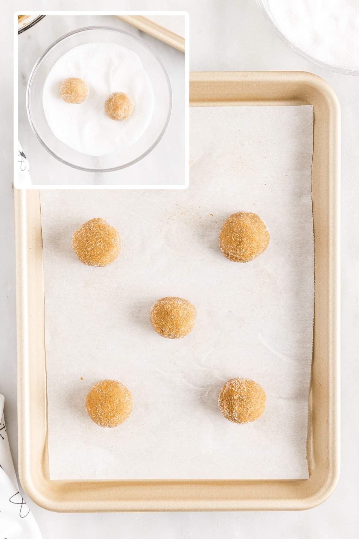 Molasses crinkle cookie dough balls rolled in sugar and placed on baking sheet lined with parchment paper.
