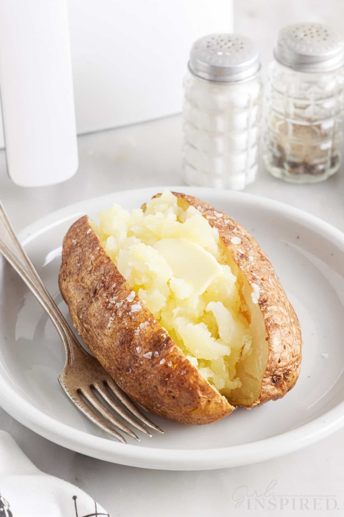 air fryer baked potato on a white plate with a fork