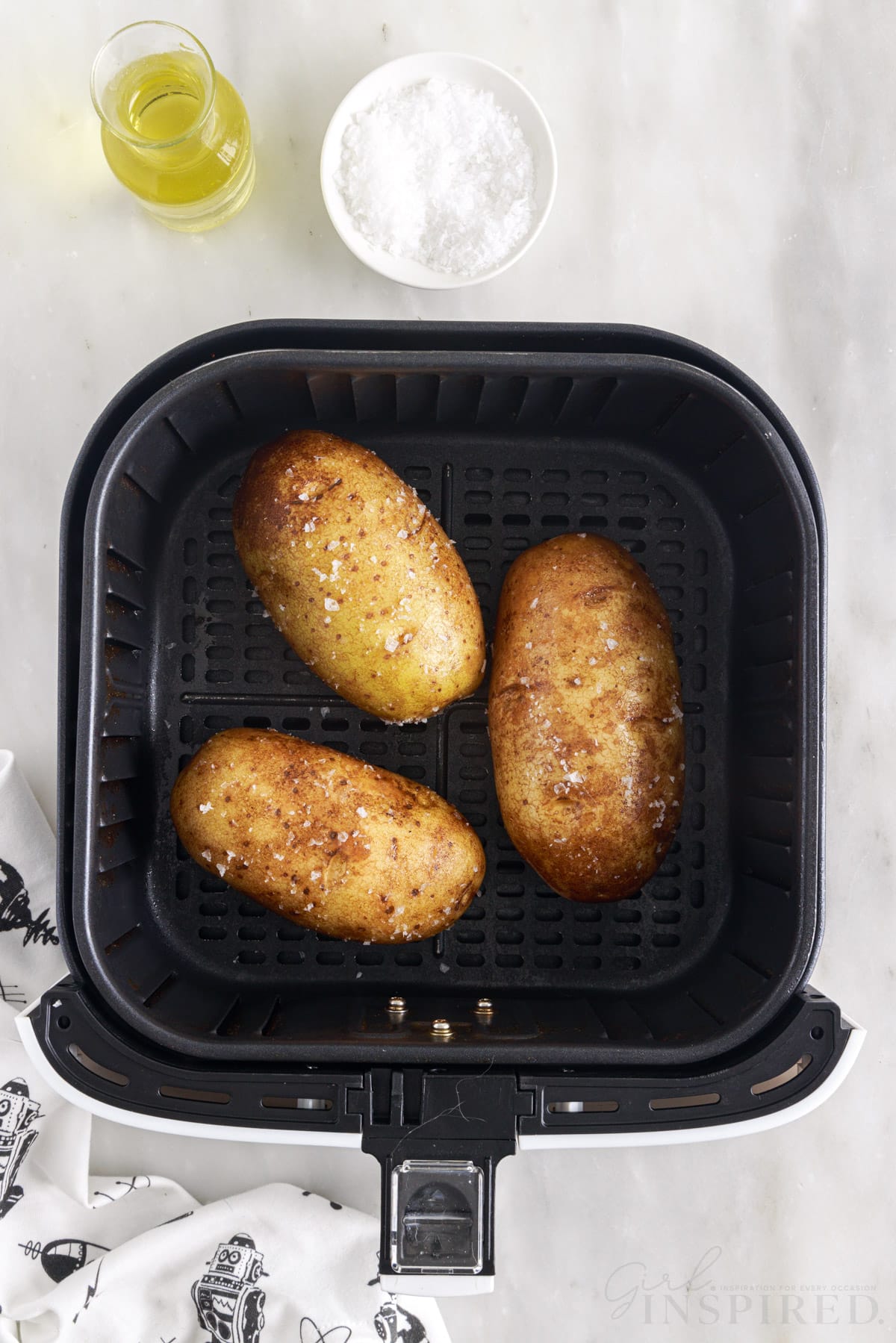 three russet potatoes in an air fryer basket before cooking