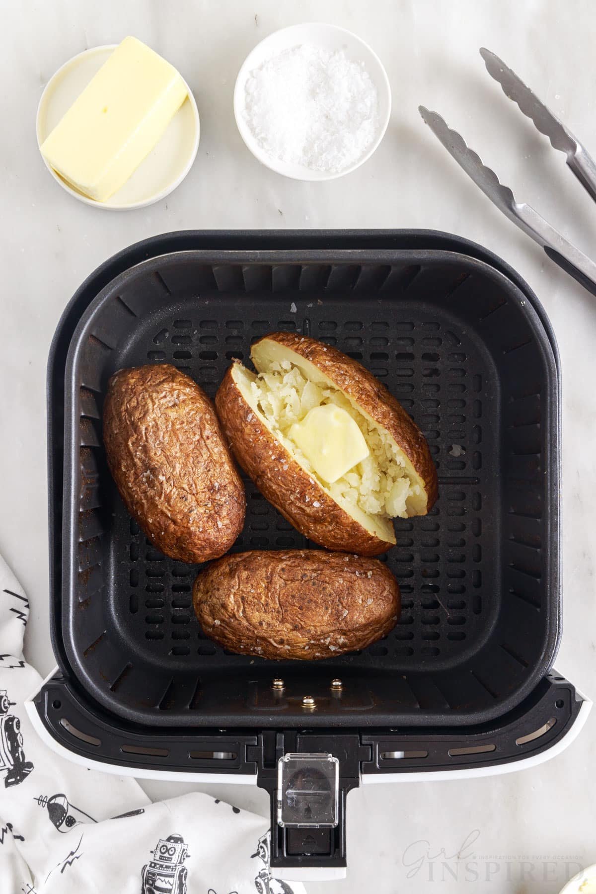 baked potatoes in the air fryer with one sliced open with a pat of butter